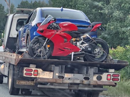 Une moto Ducati rouge se trouve derrière une berline bleue sur le pont plat d'une dépanneuse