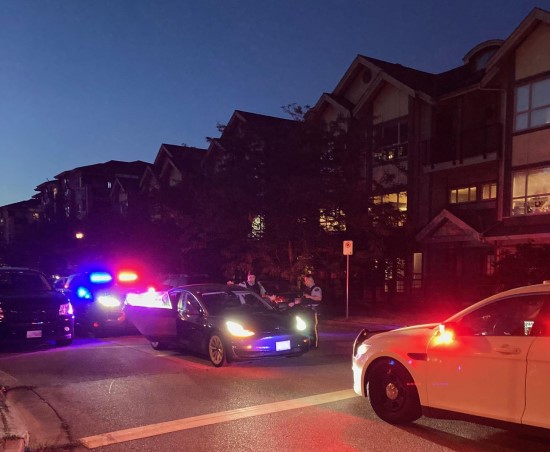 Two police vehicles with lights on sandwiching a vehicle while two officers conduct vehicle check