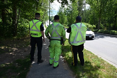 Un agent chargé de l’application des règlements et deux policiers en uniforme jaune réfléchissant se tiennent sur le bord d’une route.