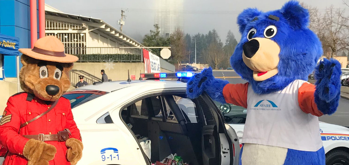 RCMP Safety Bear with the Share Society Bear standing in front of a marked RCMP vehicle